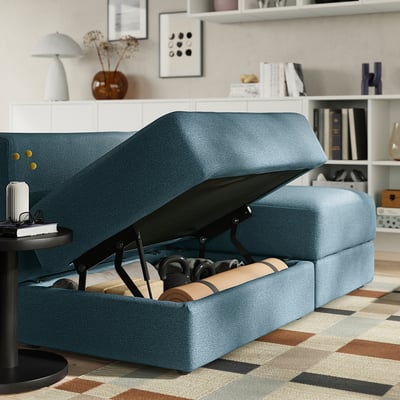 Blue JÄTTEBO sofa with an open chaise storage compartment revealing blankets and a yoga mat. The sofa gas spring dampers to support smooth opening.