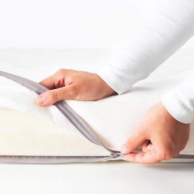 Image shows hands zipping up a cot mattress for easy cleaning.
