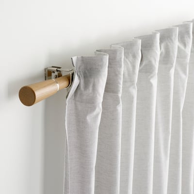 Light wooden curtain rod with metal accents, holding gathered white curtain on wall.