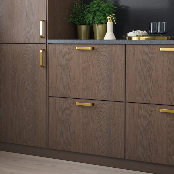 Dark brown wooden kitchen cabinets with gold handles, sleek and modern, featuring small green potted plants and decorative items on the countertop.
