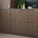 Dark brown wooden kitchen cabinets with gold handles, sleek and modern, featuring small green potted plants and decorative items on the countertop.