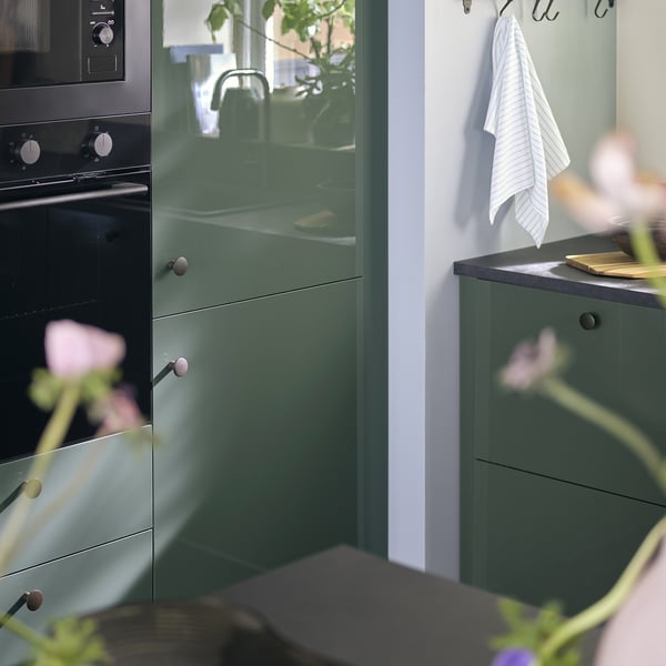 Modern kitchen with KALLARP high-gloss green cabinets, black oven, striped towel, and plants.