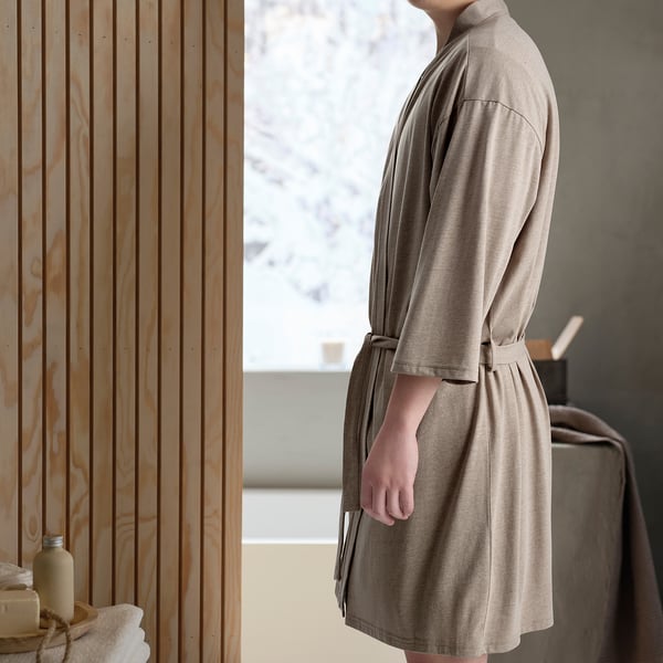 Beige KÄRRFIBBLA bathrobe with belt, pockets, mid-calf length; bathroom with wooden accents and window.