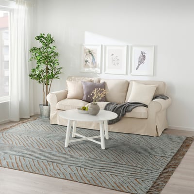 The living room a beige KLAPPERSTARR rug, larger than the white coffee table and cream sofa, with intricate textured wool and cotton design.
