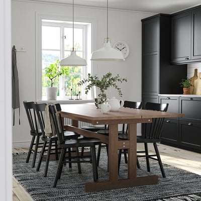 KLIMPFJÄLL dining set with large wooden table, six dark chairs, two pendant lamps, and a rug in a kitchen with natural light.