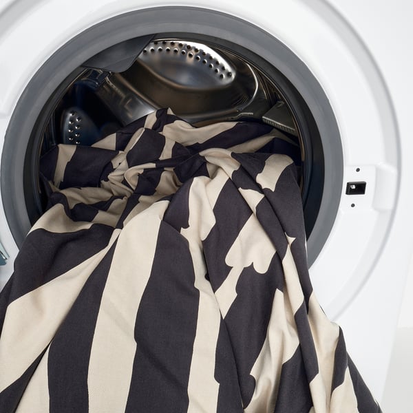 Black and white striped blanket partially inside a washing machine, showing easy-to-wash feature.