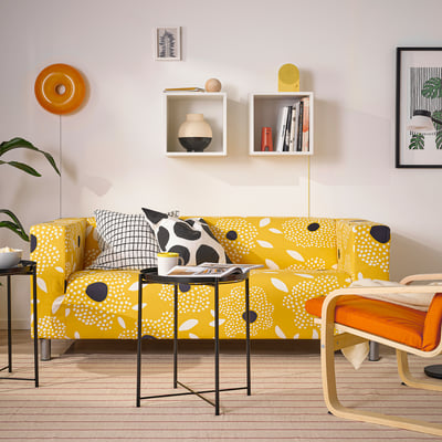 Yellow KLIPPAN sofa with polka dots, black/white pillows, orange chair, and wall shelves.