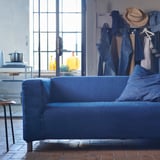 Bright living room with blue KLIPPAN sofa, denim clothes rack, and large windows.