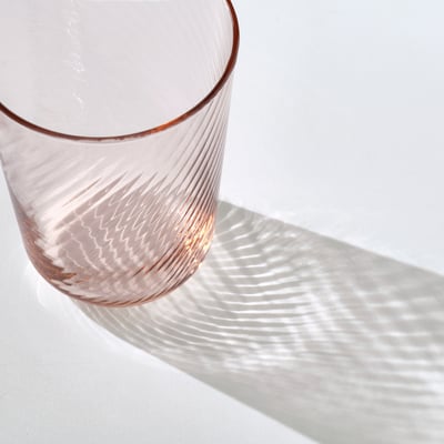 Elegant glass cup named KLIPPLAX, clear with light orange hues, sleek and streamlined shape, smooth exterior and rippled interior texture.