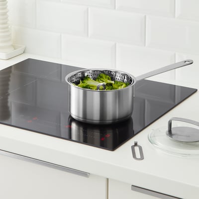 Stainless steel KLOCKREN steamer insert with handle on modern stove, steaming green vegetables.