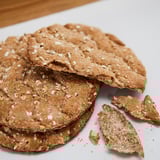 Seven brown multigrain crackers on white plate, some broken.