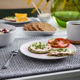 Multigrain toast, yogurt, veggies, fruit, granola, coffee on black & white placemat.