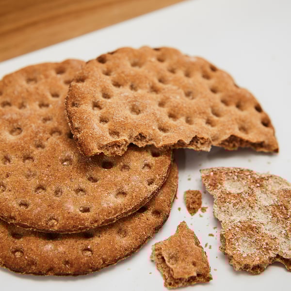 Stacked whole grain crispbreads, some broken, on white surface.