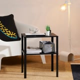 Black side table with books, felt bin, and leopard print pillow next to white couch on brown carpet.