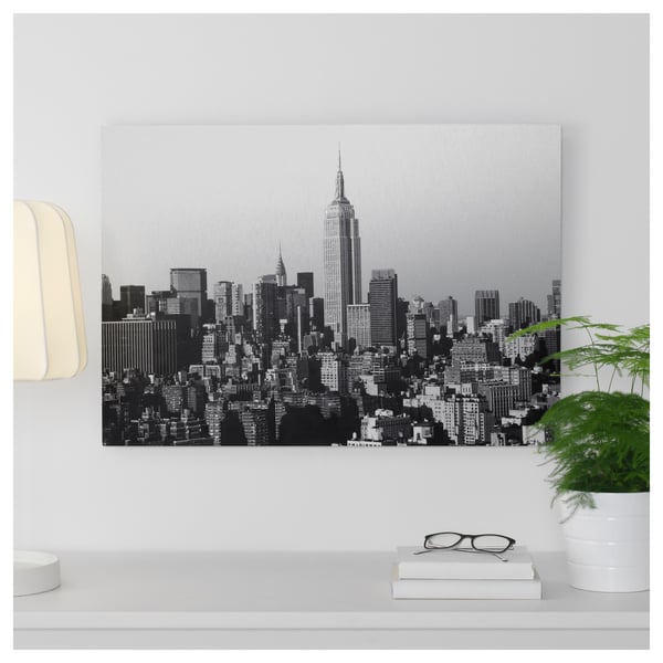 Black and white cityscape photo print on metal, displayed above a white shelf with a plant and books.