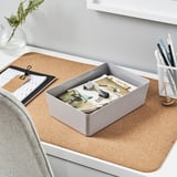 A KUGGIS gray organizer sits on a cork desk mat, containing office supplies and positioned near a pen holder and notebook.