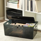 Plastic storage box with lid on carpet near bookshelf. Holds papers and small items. Part of the KUGGIS series.