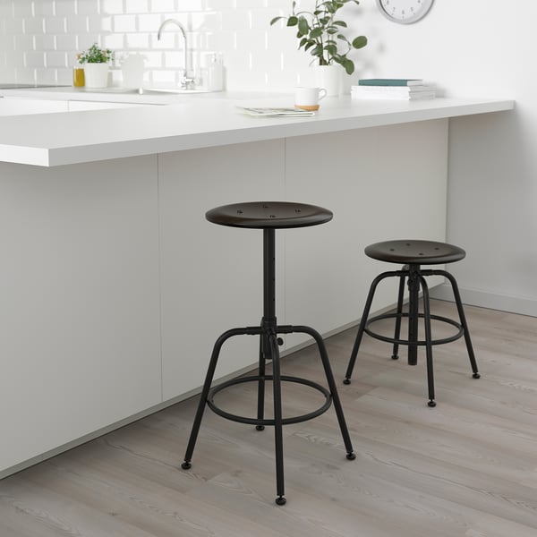 Two KULLABERG stools beside kitchen island, one adjustable for under-counter use, both with metal footrests and birch tops.