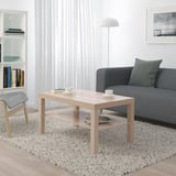 Minimalist living room: LACK coffee table, gray sofa with green pillow, white bookshelf, floor lamp.