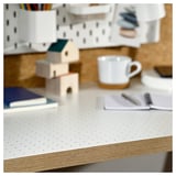White desk with perforated top, wooden blocks, blue book, white mug, and notebook with pen.