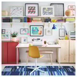 Bright home office setup with light wood desk, yellow chair, colorful art, and blue rug. Modern and fresh design.