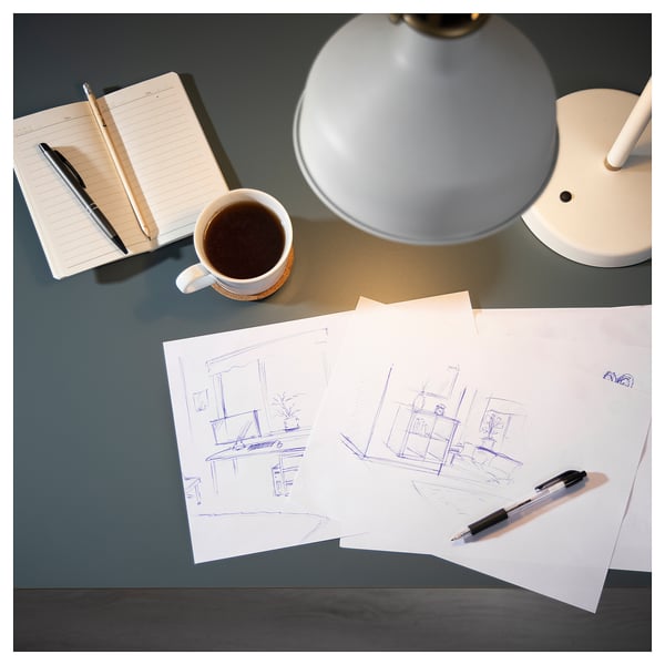 Blue desk with white lamp, notebook, pens, and sketches. Coffee cup beside.