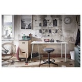 Industrial-themed workspace with white desk, grey stool, bikes, and wall art.