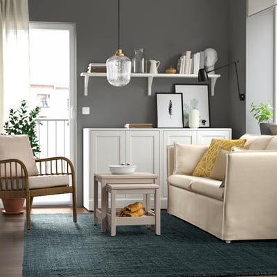 Modern living room with LANDBANA jute rug, two armchairs, sofa, and decor on grey wall shelves, creating a cozy atmosphere.