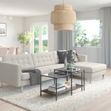 Modern living room with white l-shaped LANDSKRONA sofa, gray throw, glass coffee table, and large window. Stylish, minimalist decor.