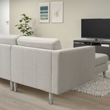 Modern gray 3-seat sofa in living room with metal legs, cushioned seats, rug, tv, plant.