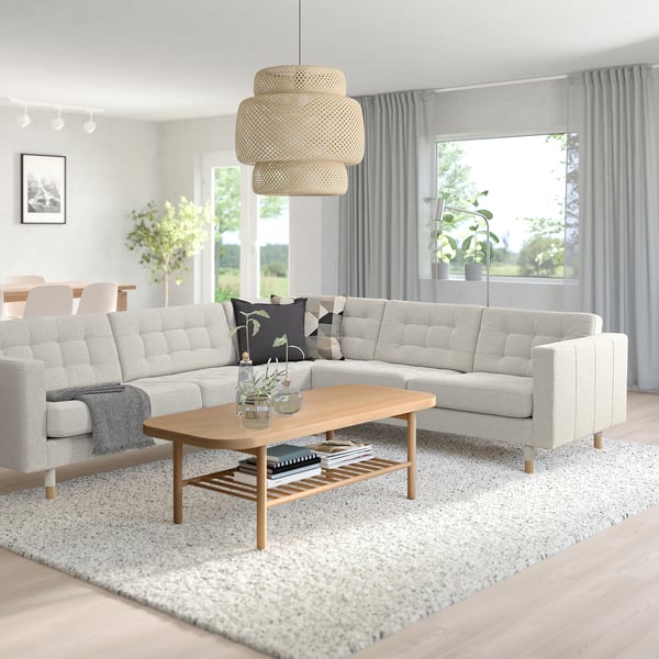 Modern living room with light grey l-shaped sofa, wooden coffee table, and pendant lamp. Grey curtains frame windows, letting in natural light.