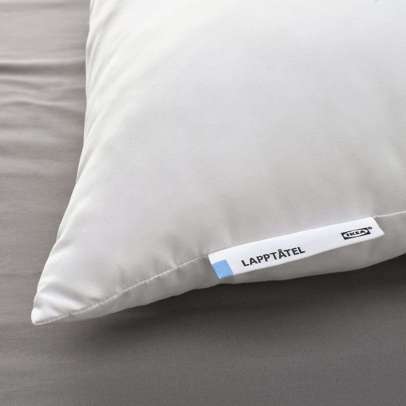 White plush pillow labelled LAPPTÅTEL on bed, soft and inviting with smooth fabric and stitched edges.