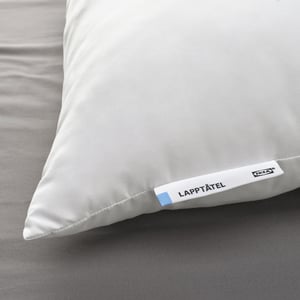 White plush pillow labeled LAPPTÅTEL on bed, soft and inviting with smooth fabric and stitched edges.
