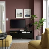 Modern living room with dark purple walls, yellow couch, flat screen tv on black stand, green plant, and framed nature pictures.