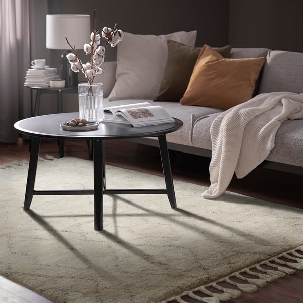 Cozy living room with black coffee table, white flowers, gray sofa, and warm lighting.