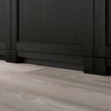 Black wooden baseboard for kitchen cabinets, resting on light wooden floor.