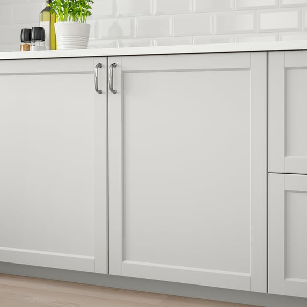 Light grey kitchen cabinets with beveled edges and handles, fitted to wooden floor and white tiled backsplash.