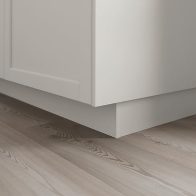 White wooden kitchen cabinet plinth on light wooden floor.