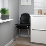 Black office chair with metallic legs next to white cabinet. Different decorative items are placed on shelves.