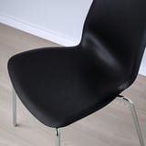 Black modern chair with sleek, curved design and chrome legs on a wooden floor.