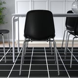 Modern black chair with chrome legs, stacked on patterned floor.