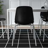 Three modern chairs with black seats and metal legs are arranged around a white table on a black grid floor. They are stackable and easy to clean.