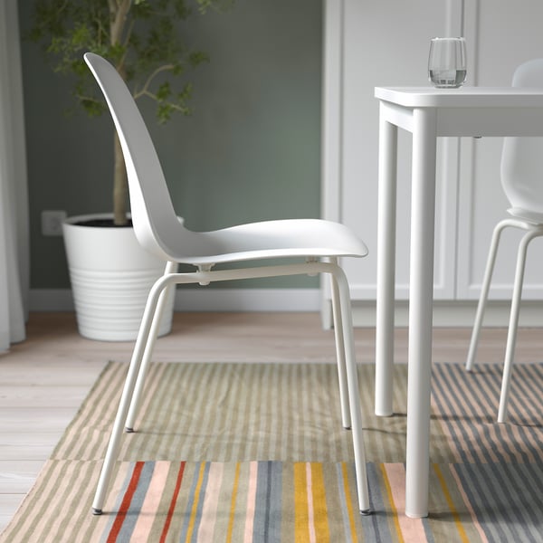 Modern white chair with angular back, sitting on a striped rug, beside a small white table.