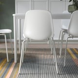 Three modern white chairs arranged around a small table on a striped rug. The chairs have flexible backrests and can stack for space-saving.