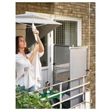 Woman adjusts beige LILLEÖ parasol on balcony with green table and chair.