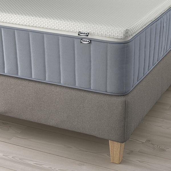 Ikea LILLFJÄLLET bed with cushioned headboard, grey. Mattress shows side stitching and ikea tags, on wooden floor.