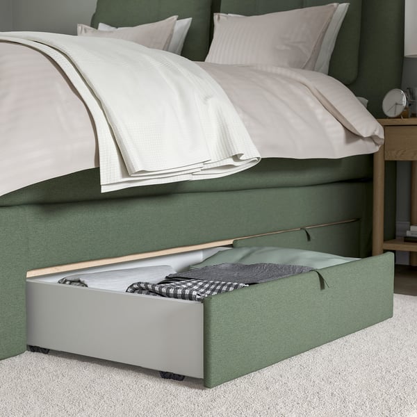 A green divan bed with open storage drawers under a folded blanket.