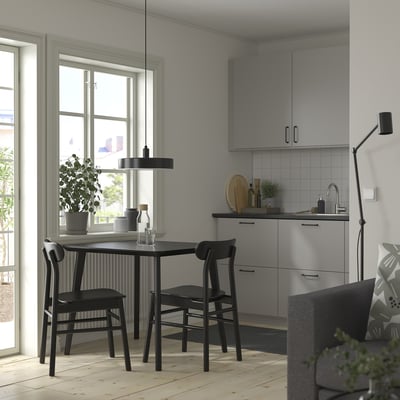 Modern kitchen nook with LISABO black table, wooden-legged chairs, grey cabinets, white backsplash, plants, and pendant light.