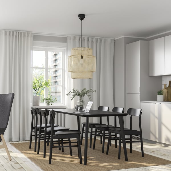 Modern dining room with LISABO black table and six chairs, under a pendant light, with tall windows and plants.