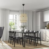 Modern dining room with LISABO black table and six chairs, under a pendant light, with tall windows and plants.